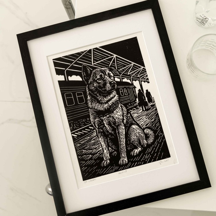 Linoryt czarno bialy przedstawiajacy psa "Hachiko" w ramc